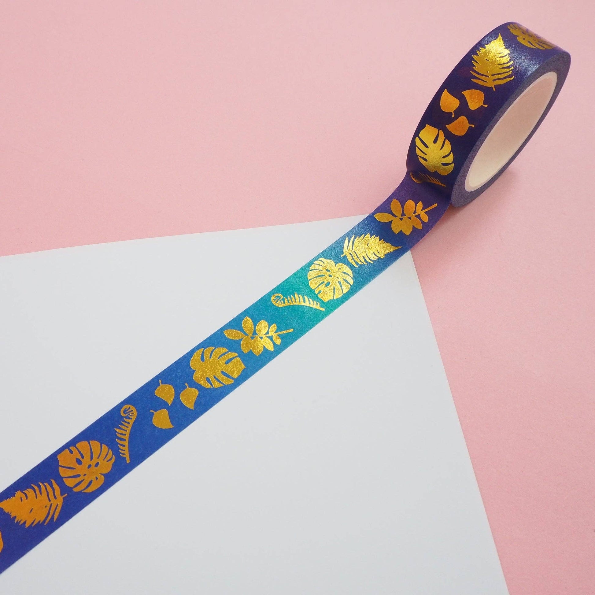 A roll of washi tape with a tropical leaf pattern, shown partially unrolled over a diagonal split background of pink and white.