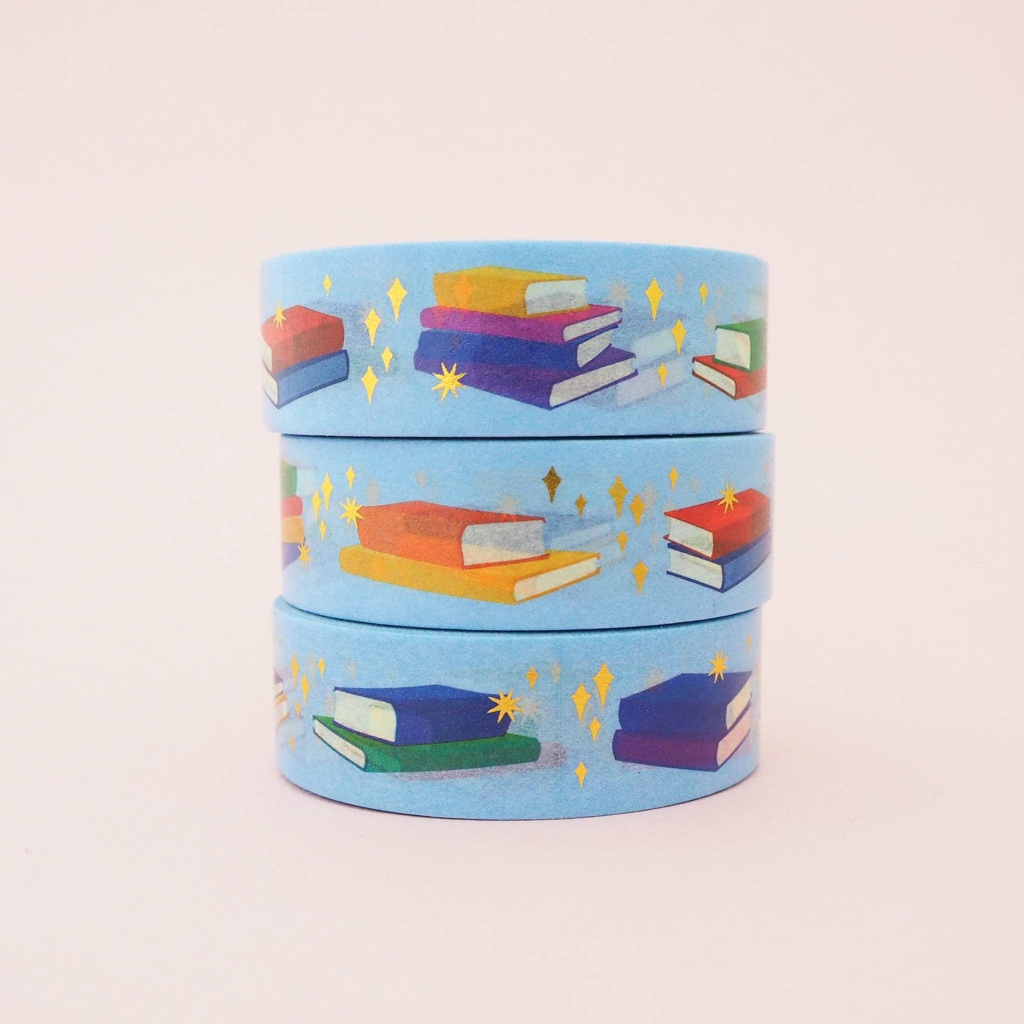 3 rolls of washi tape, light blue with a repeated pattern of different colour stacks of books on a pale pink background.