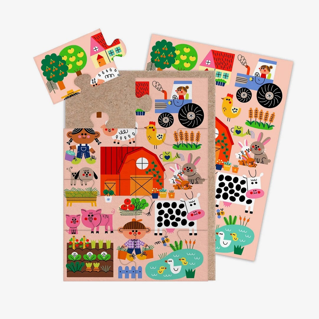 A jigsaw greeting card featuring colourful illustration of a farm yard on a pale pink background, with a brown kraft paper envelope visible on the left side, on a clean white background.
