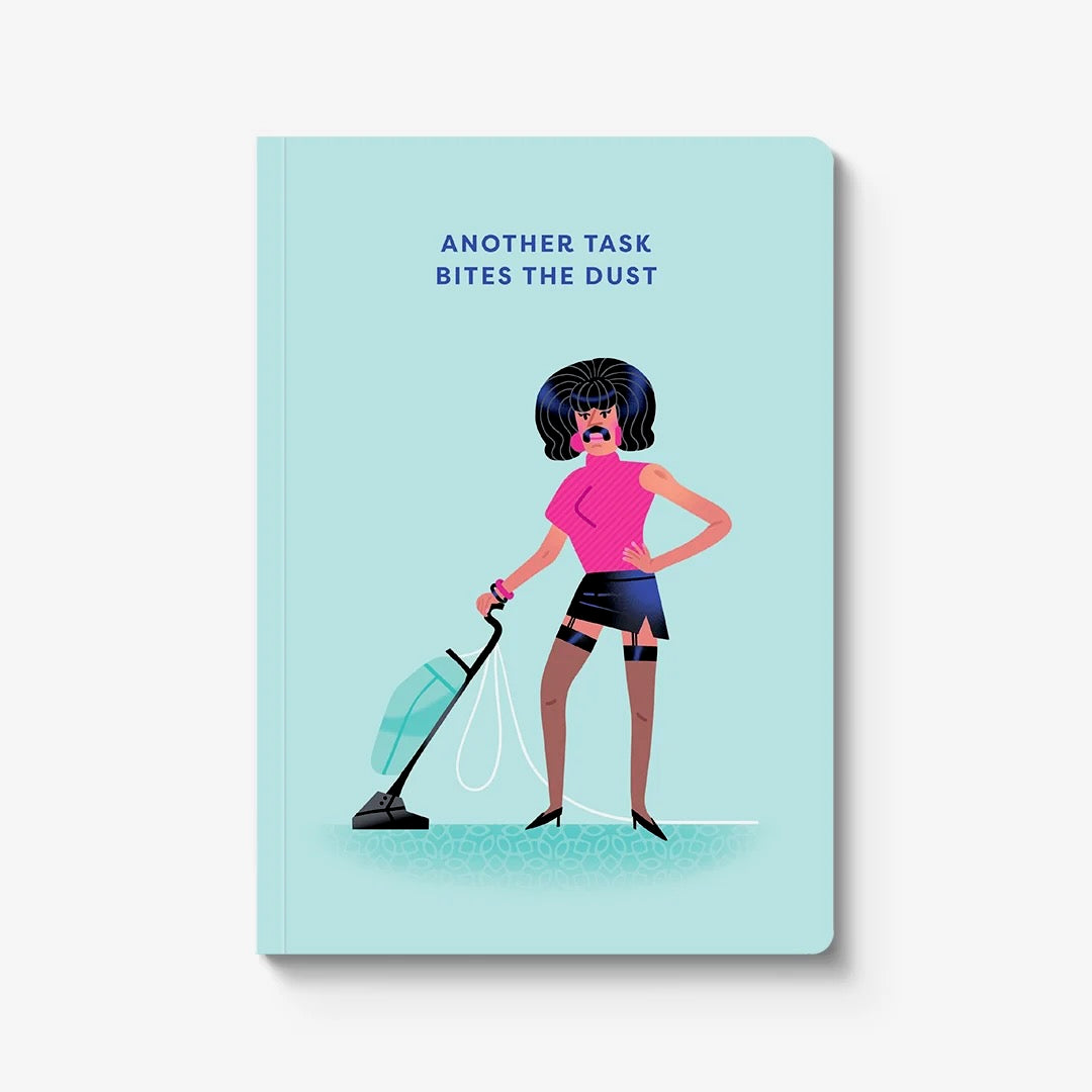 A hardcover notebook with a light blue cover, featuring a flat vector illustration of a Freddy Mercury like figure vacuuming and the text 'ANOTHER TASK BITES THE DUST' in dark blue. The notebook is shown standing upright against a clean white background with a soft drop shadow.