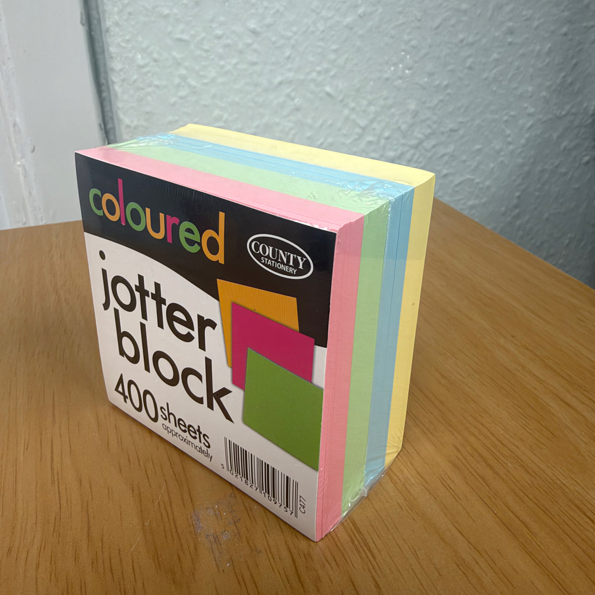 Picture of a jotter block on a table, showing the different colours of the pages; pastel pink, green, blue and yellow.