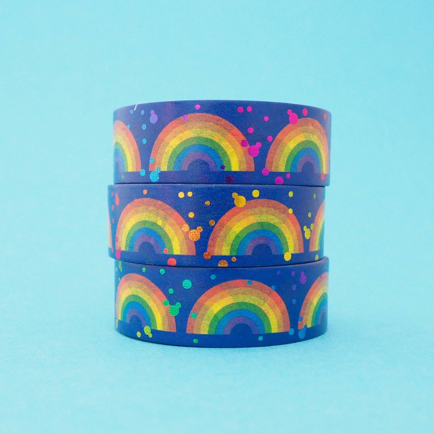Three rolls of washi tape, with a repeated pattern of rainbows and multicoloured dots on am aqua background.