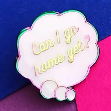 A cloud-shaped enamel pin with the phrase 'Can I go home yet?' in gold script, with an iridescent trim, shown against a split blue and magenta background.