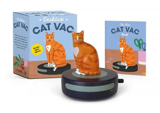 A Photo of the Cat Vac Box with the catvac in front of it, a mini robot vacuum with a ginger cat on top and the accompanying book in the background.
