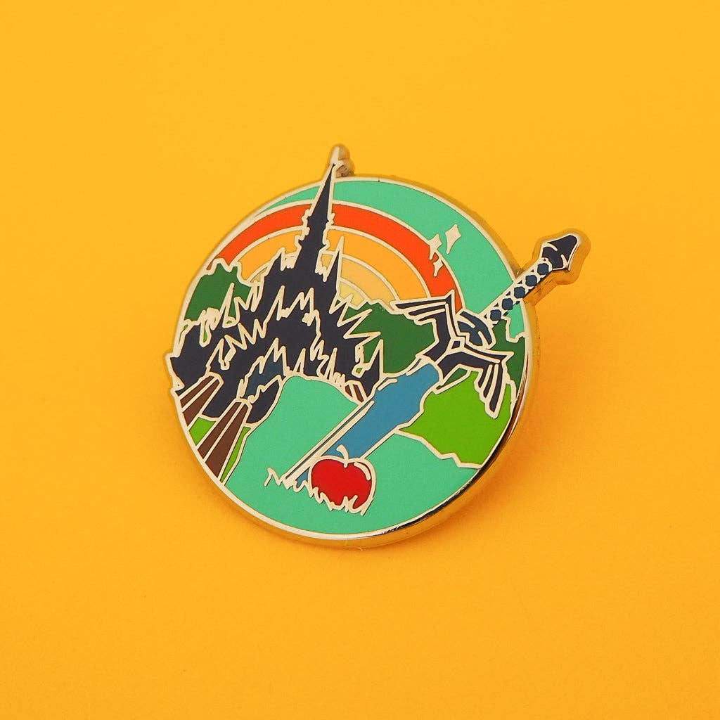 Colorful enamel pin with a design of a sword, heart, and castle on a yellow background