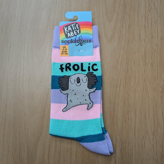 A photo of a pair of striped lilac, pink, mint green and dark teal socks, featuring a cartoon koala beneath the word "FROLIC"