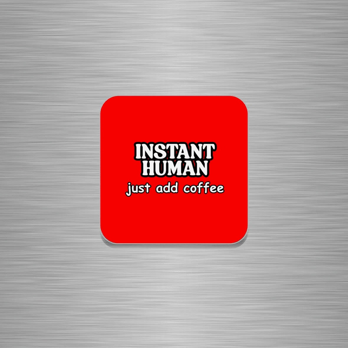 A square red fridge magnet with rounded corners featuring the text 'INSTANT HUMAN' in white with black outlines and 'just add coffee' underneath, shown on a brushed silver metal background.
