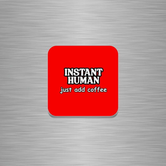 A square red fridge magnet with rounded corners featuring the text 'INSTANT HUMAN' in white with black outlines and 'just add coffee' underneath, shown on a brushed silver metal background.
