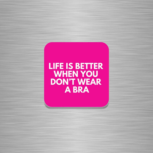 A square pink fridge magnet with rounded corners, featuring the text "LIFE IS BETTER WHEN YOU DON'T WEAR A BRA"  in white, shown centred on a brushed silver metal background.