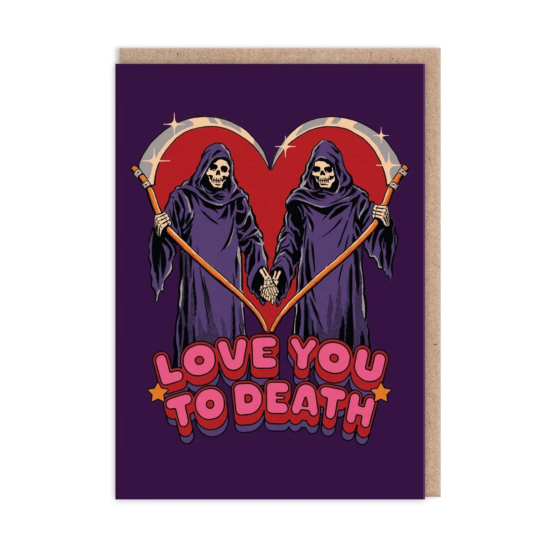 A greeting card with a kraft paper envelope, featuring a dark purple background and a graphic of two grim reapers holding scythes that form a heart shape. Below them is the text 'LOVE YOU TO DEATH' in pink and red bubble letters.