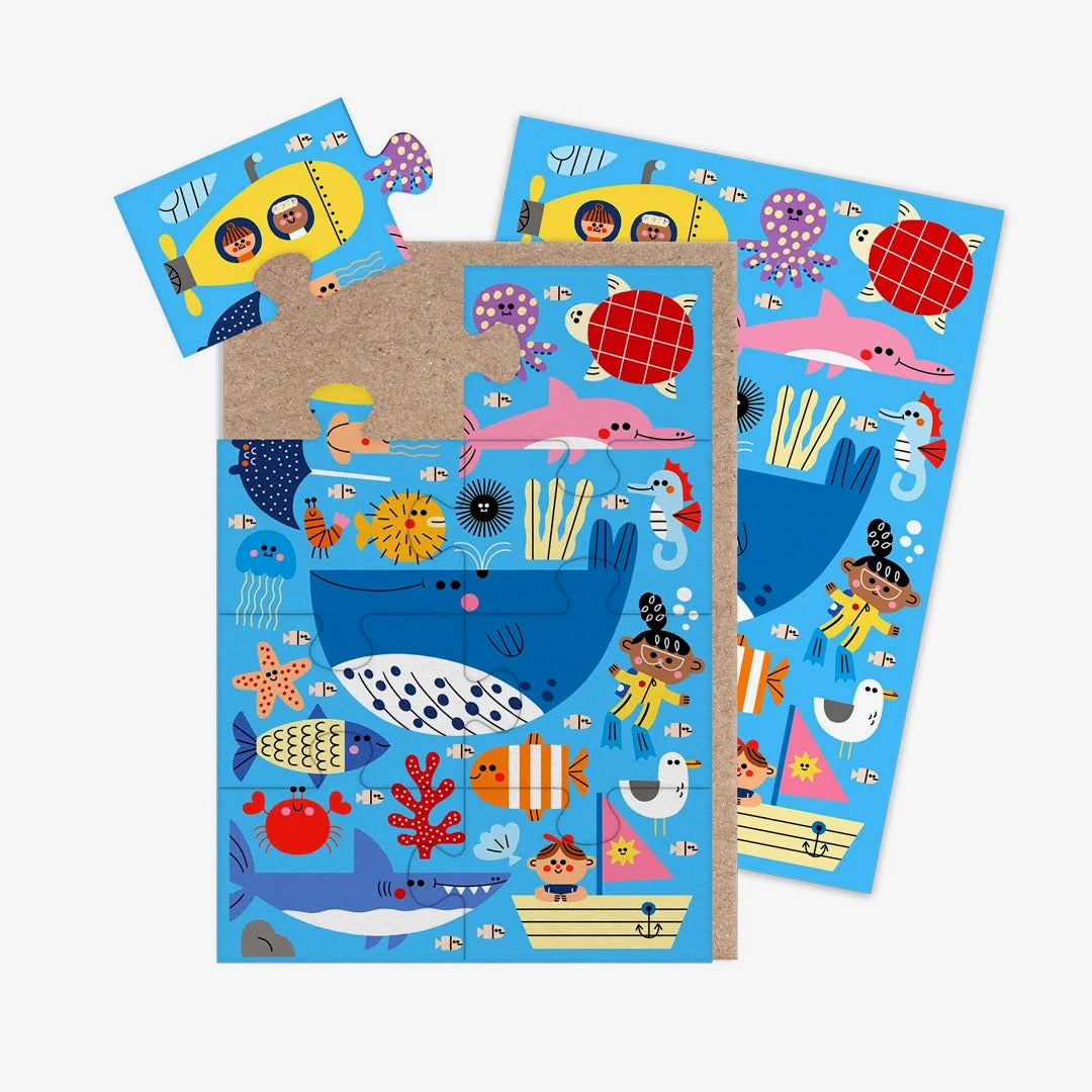A jigsaw greeting card featuring colourful illustration of sea life on a light blue background, with a brown kraft paper envelope visible on the left side, on a clean white background.