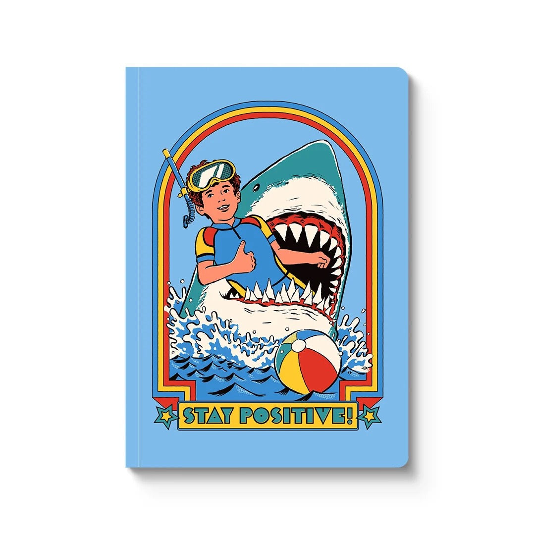 Notebook with a retro illustration of a shark and a boy in its mouth on a blue background, with the text 'Stay Positive!'.