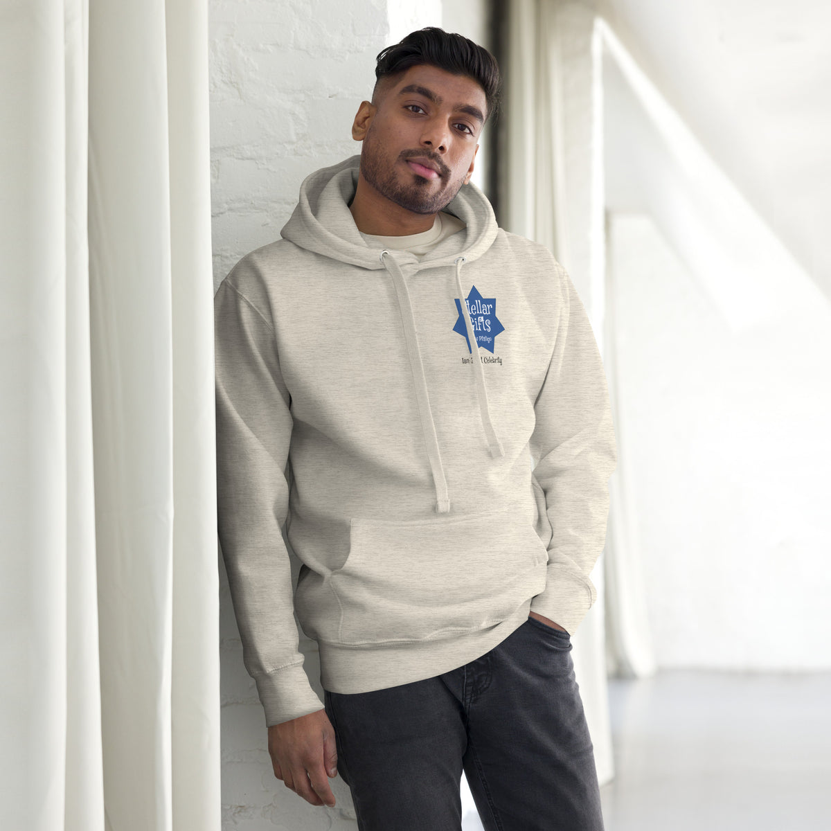 A man wearing a light brown hoodie, shot from the front on a light background. The hoodie has a dark blue, seven-sided star on the chest with the STELLAR GIFTS logo written in it in white text, with "New Pitsligo" written below it.