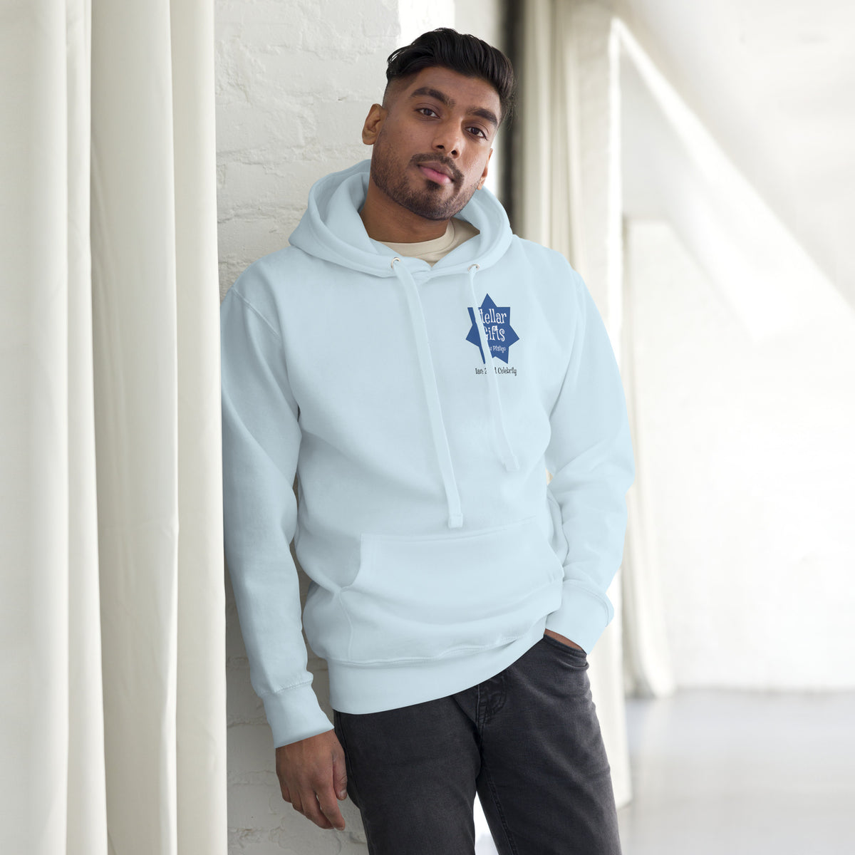 A man wearing a light blue hoodie, shot from the front on a light background. The hoodie has a dark blue, seven-sided star on the chest with the STELLAR GIFTS logo written in it in white text, with "New Pitsligo" written below it.
