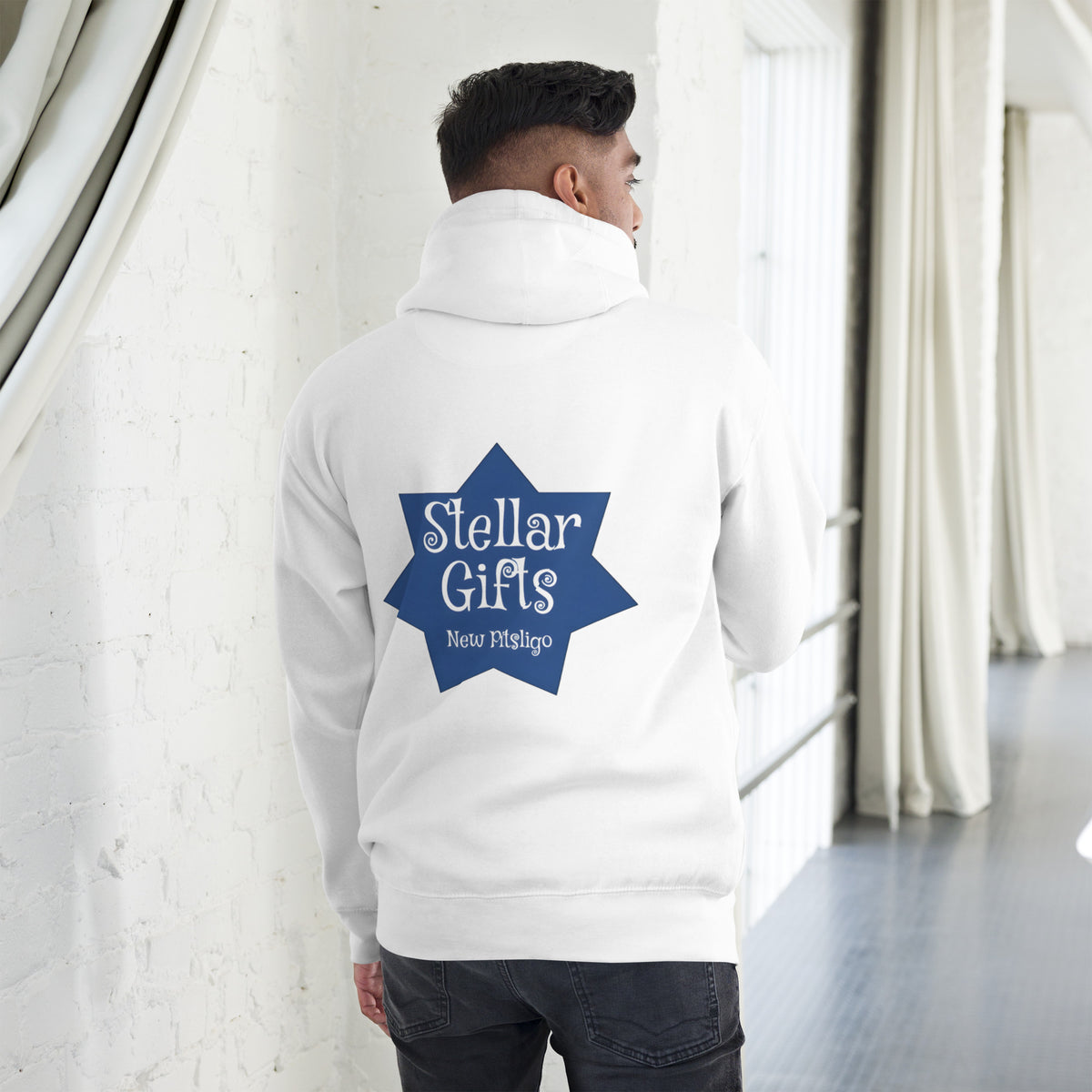 A man wearing a white hoodie, shot from behind on a light background. The hoodie has a dark blue, seven-sided star on the back with the STELLAR GIFTS logo written in it in white text, with "New Pitsligo" written below it.