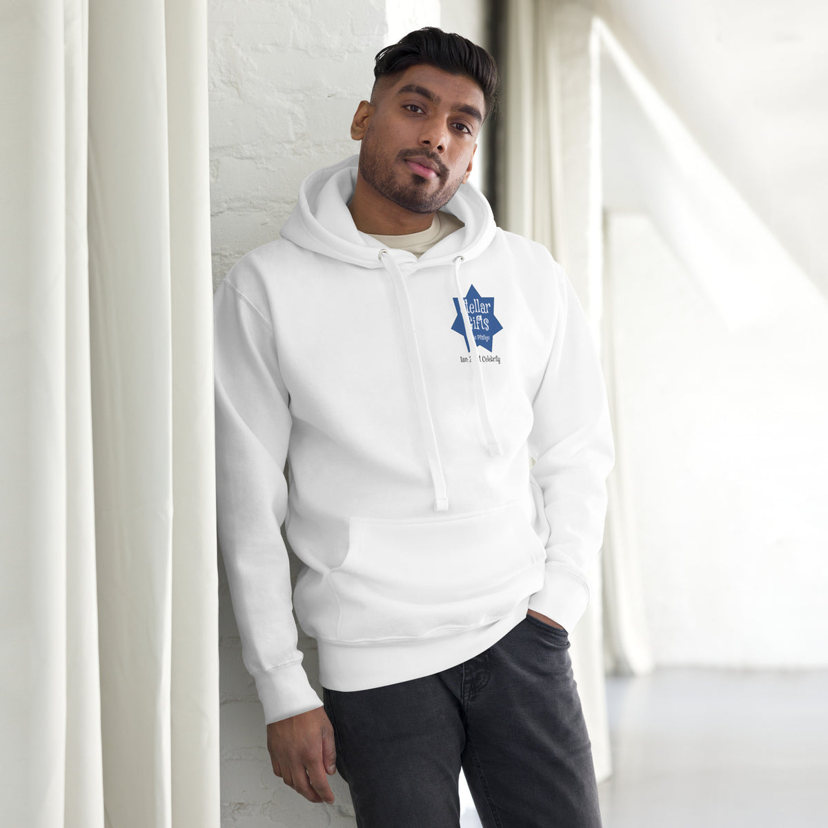 A man wearing a white hoodie, shot from the front on a light background. The hoodie has a dark blue, seven-sided star on the chest with the STELLAR GIFTS logo written in it in white text, with "New Pitsligo" written below it.
